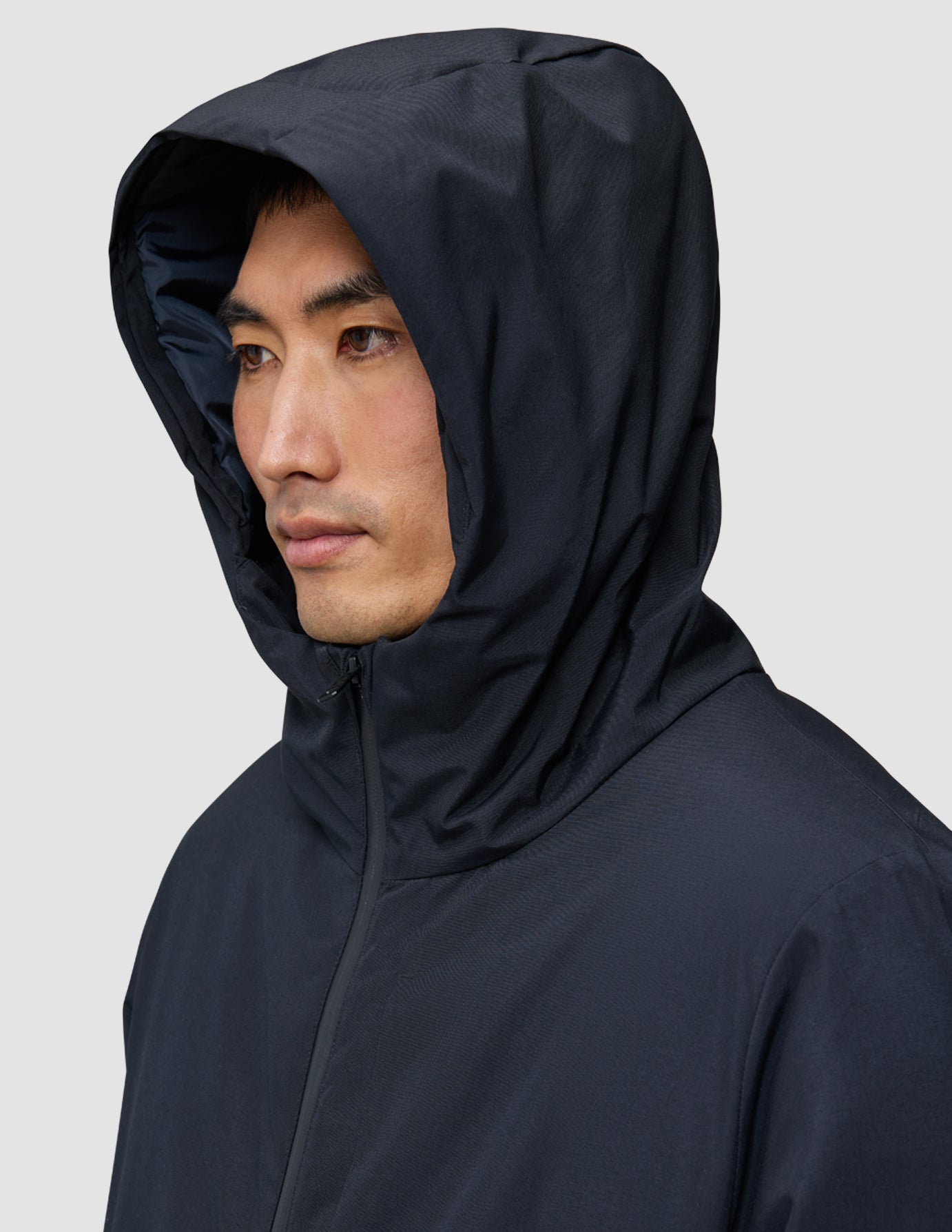 En person som bär en svart Utility Jacket Black med huvan uppe, en jacka som är vind- och vattentät.